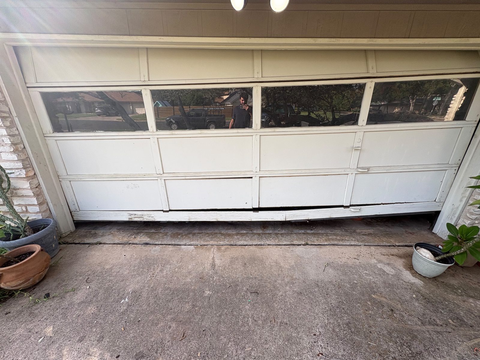 Warped and rotting wood garage door panel with a gap at the bottom on an Austin, TX home